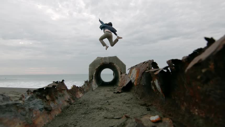 A person jumping over a structure in very slow motion near a beach