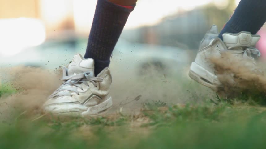 Sneakered feet slide across dirt and grass in slow motion