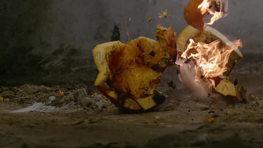 A pumpkin that was lit on fire falls and smashes on the ground