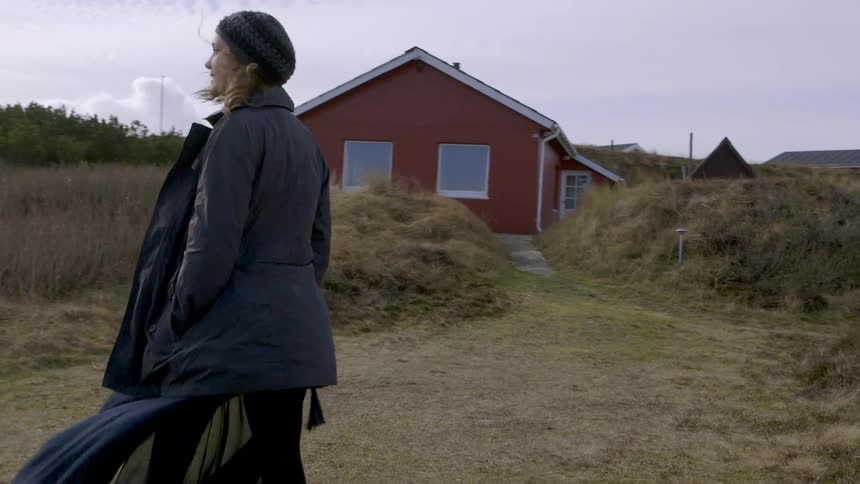 A woman walks near a house on a windy day