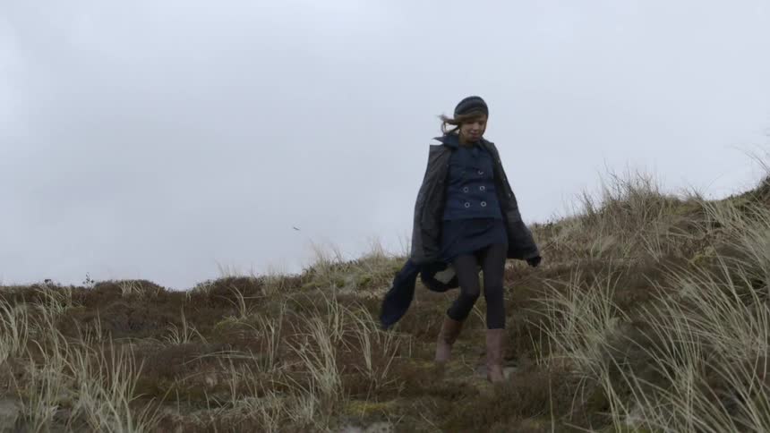 A woman walks down a grassy hill on a windy day