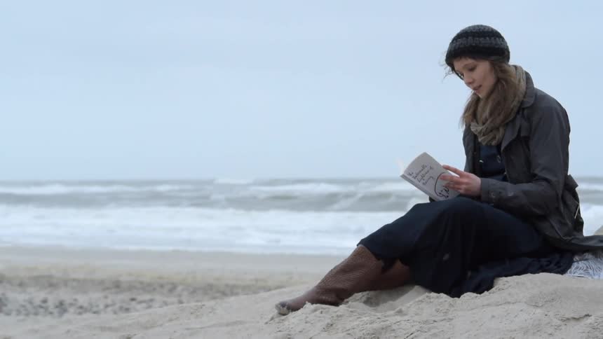 Woman sits on a beach on a windy day reading a book
