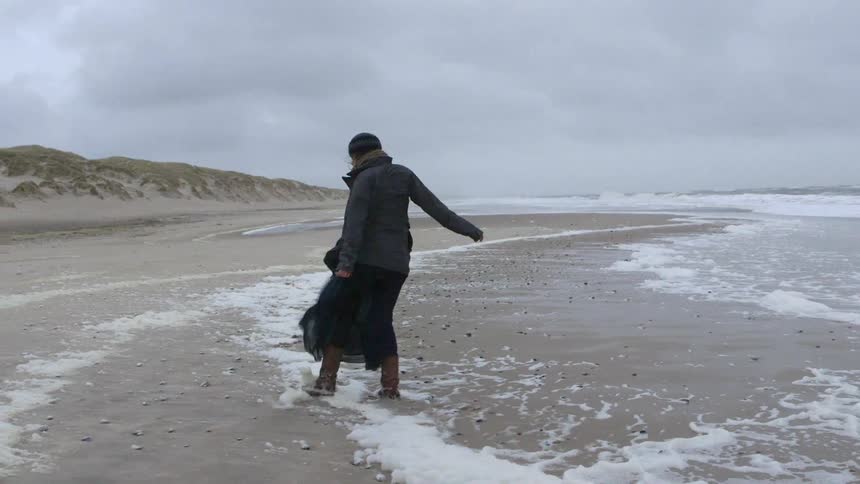 Woman dances and kicks sand on the beach