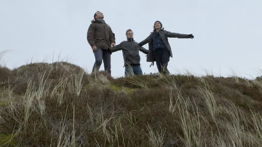 Three people stand atop a ridge shouting and enjoying themselves
