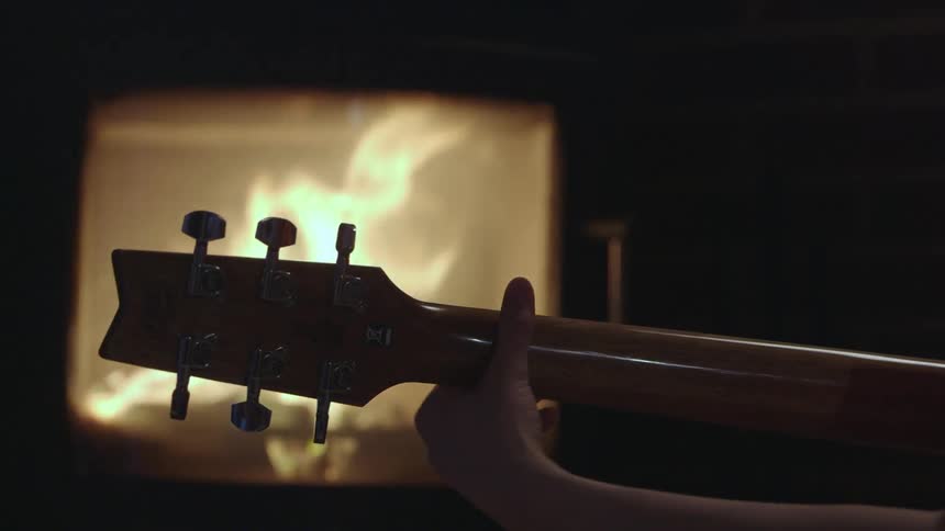 A guitar being played by a fireplace