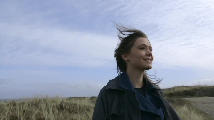 A woman stands on a windy field looking around smiling