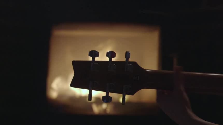 A guitar being played by a fireplace