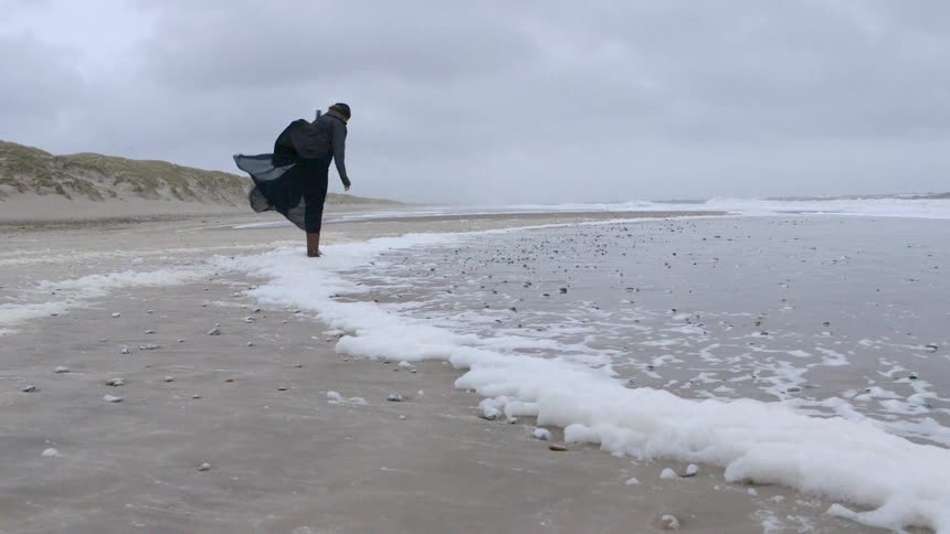 A woman kicks at foam on the beach