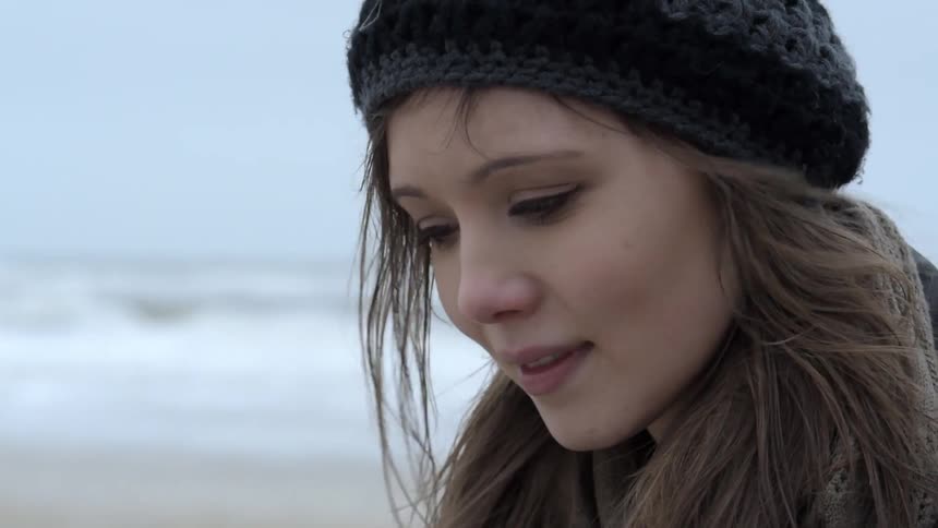 A young woman stands on a beach smiling while reading something