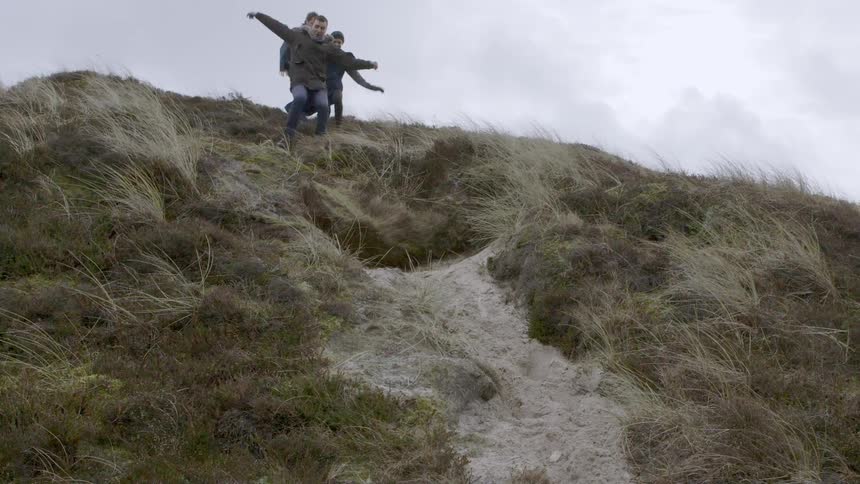 Three people sprint down a grassy hill