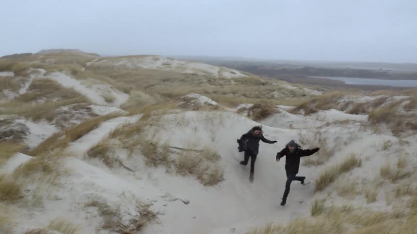 Man and woman running down sandy hills at the beach