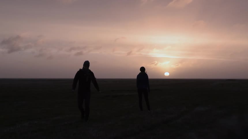 A person watching the sunset, another walks away