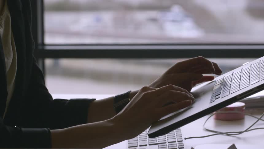 A woman sitting at a desk types on a laptop