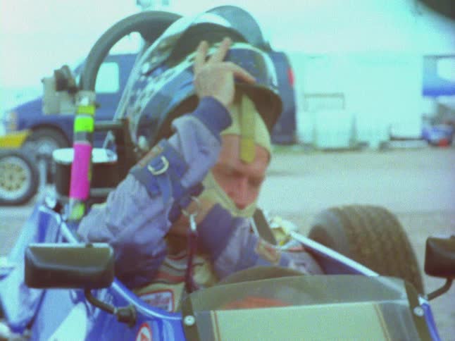 A man seated in a race car is putting on his helmet
