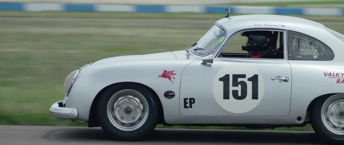 A vintage car is racing down a runway on a cloudy day