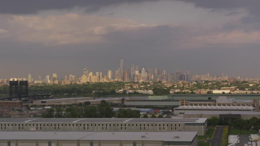On a cloudy day there is a large metropolitan city visible from beyond a dreary looking industrial area