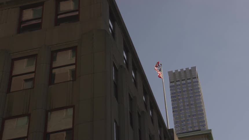 An american flag is seen flapping in the wind as it hangs from a flagpole high atop a building