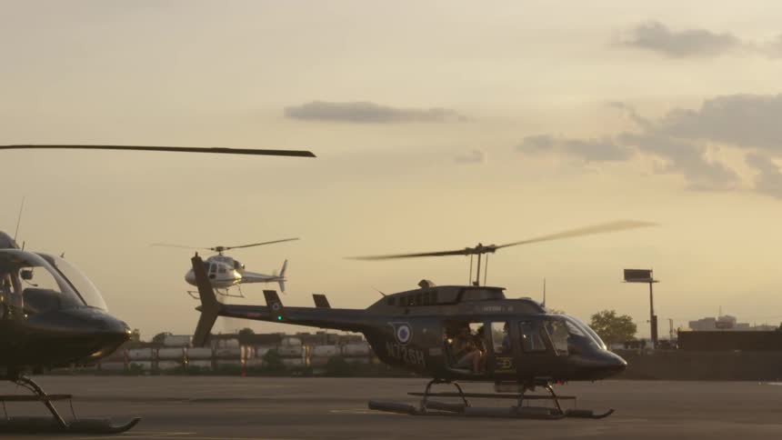 A helicopter is just touching down as another behind it is descending and a third helicopter sits stationary to the left