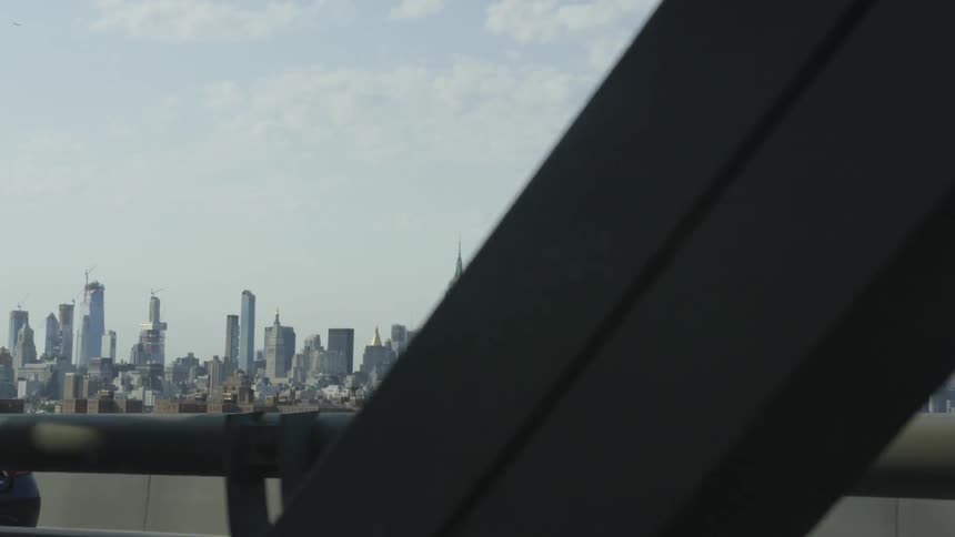 A crowded metropolitan area is visible from beyond the steel beam and cables of a nearby bridge