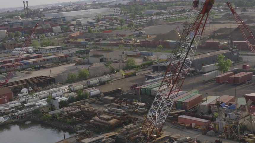 Cranes stand tall over the water with shipping containers stacked behind them
