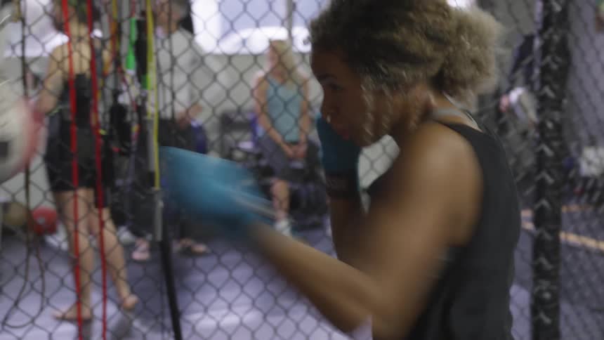 A young black woman in a tank top is practicing her jabbing on a small ball attached to elastic straps