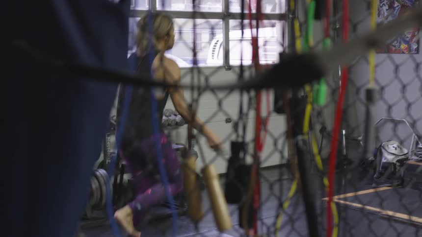 A female with bare feet is jumping rope inside the netted area of the workout room