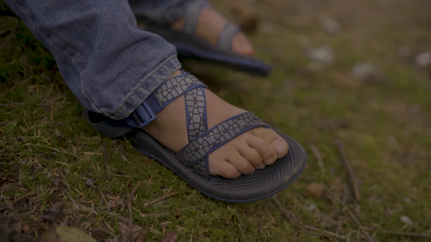 Boy wearing jeans moves his toes in slippers outdoors