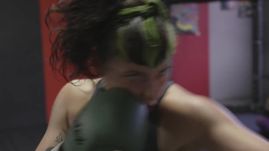 Woman punches punching bag at gym during daylight