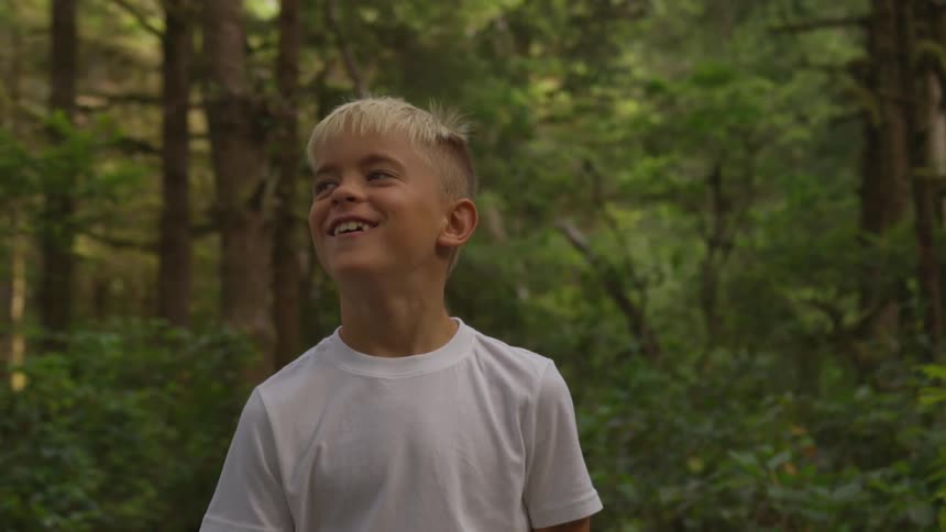 Boy wearing white t shirt walks through forest and smile during the daytime