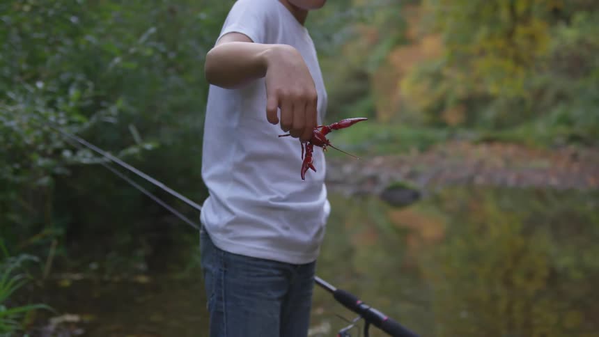 Man holds crawdad and fishing pole near river