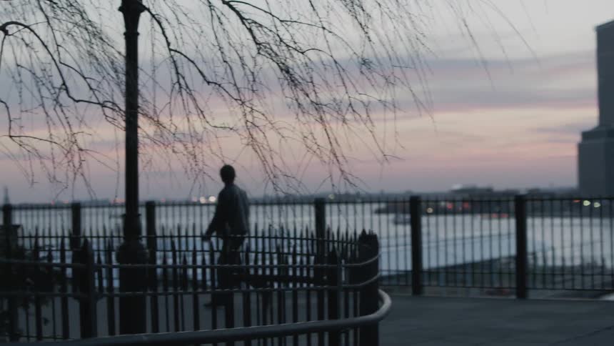 A man is looking at his phone as he walks on a pier at sunset