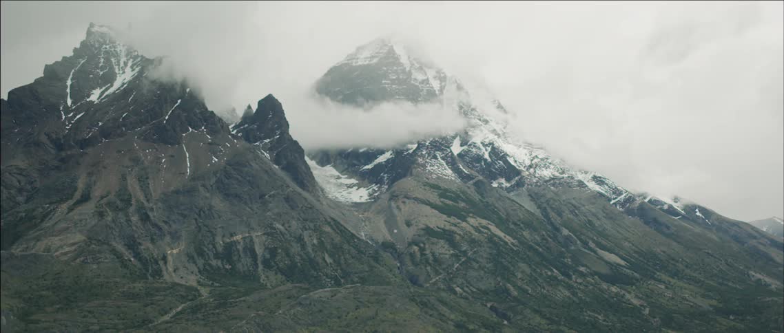 A large mountain covered in snow has clouds covering the top