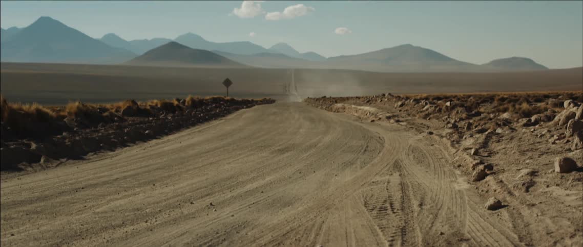 A large dirt road leads into a desert on a sunny day