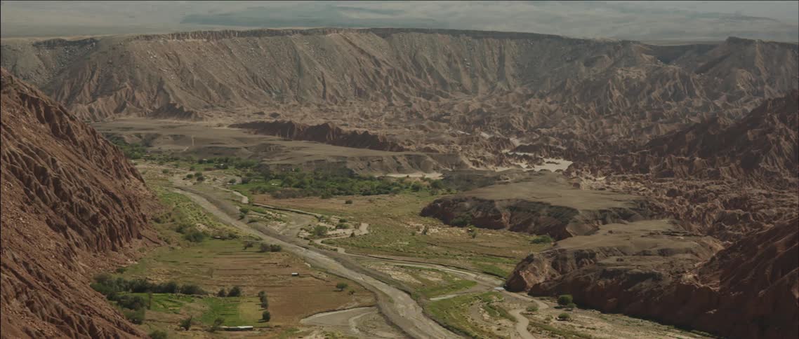 A barren valley bounded by steep hills with a narrow river running through it