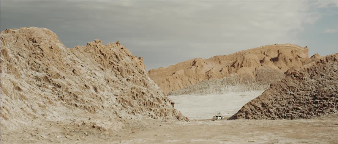 A large canyon has a vehicle with people walking around it
