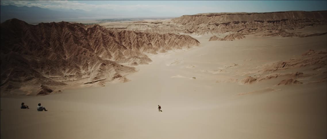 Aerial view of someone walking and stumbling through a sandy desert valley