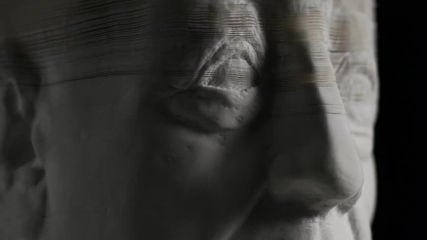 A statue slowly comes apart in a dark room