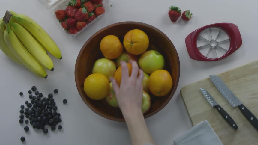 Person picks up an orange from a fruit bowl on a prep table