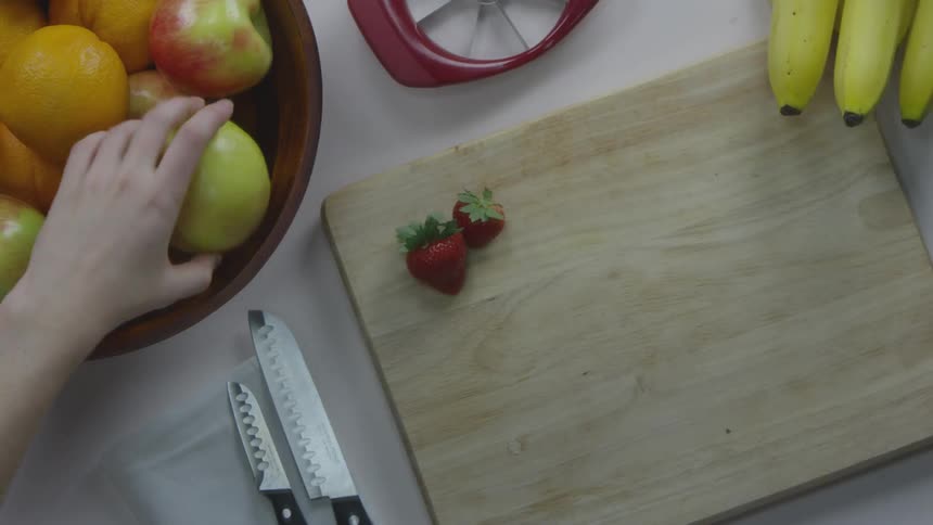 A person places an apple into a fruit bowl on a prep table