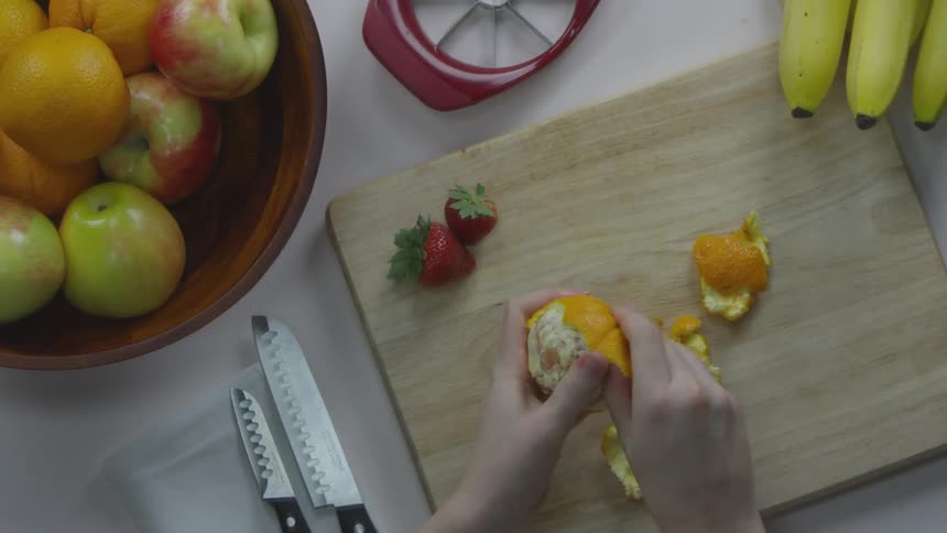 A person peels an orange on a cutting board