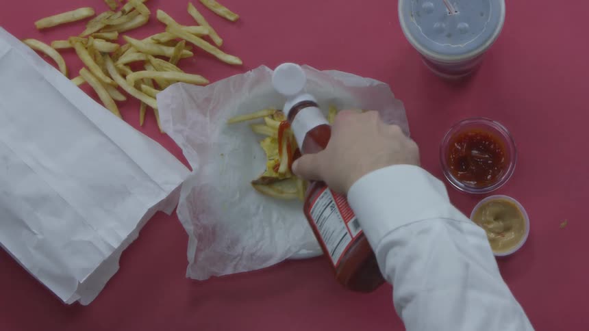 Person pulls apart a hamburger and puts fries and catsup on it