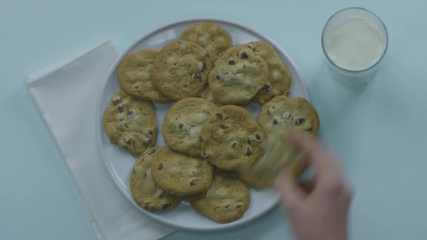A person grabbing a cookie and dunking it in milk