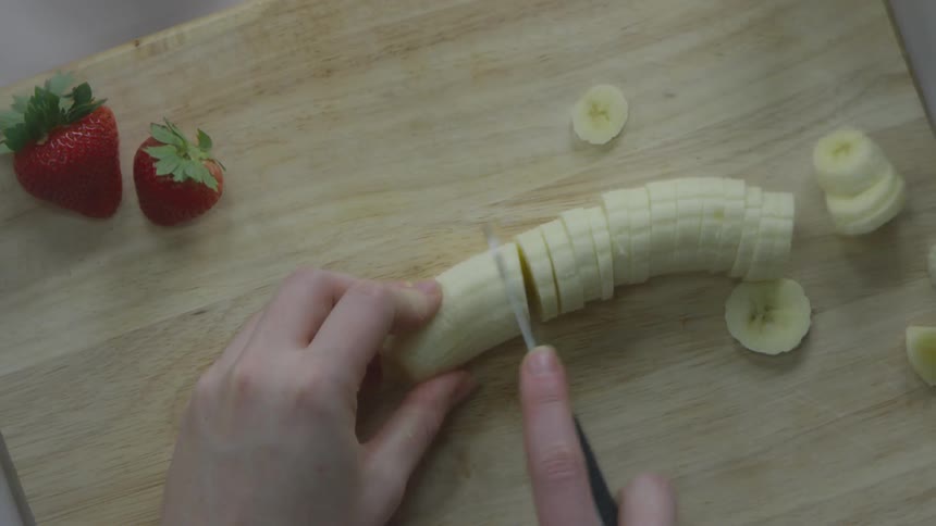 A white person slices a banana on a cutting board