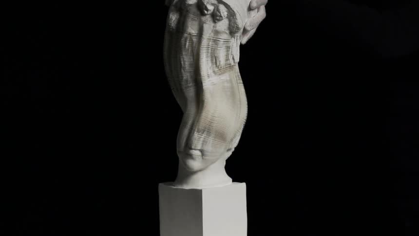 Two hands pull a large statue apart in a dark room