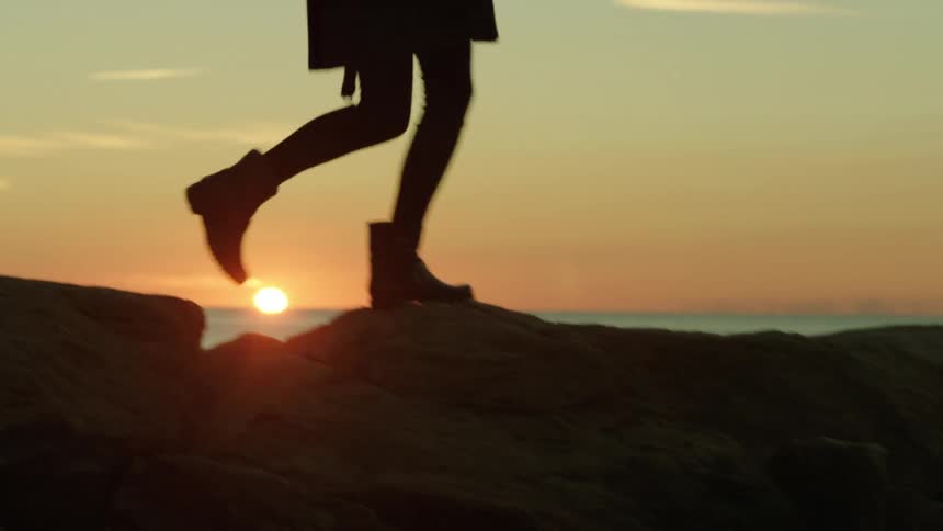 Person walking along a rocky ledge before a body of water