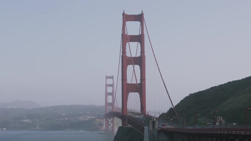 A large red bridge gaps a body of water on a foggy day