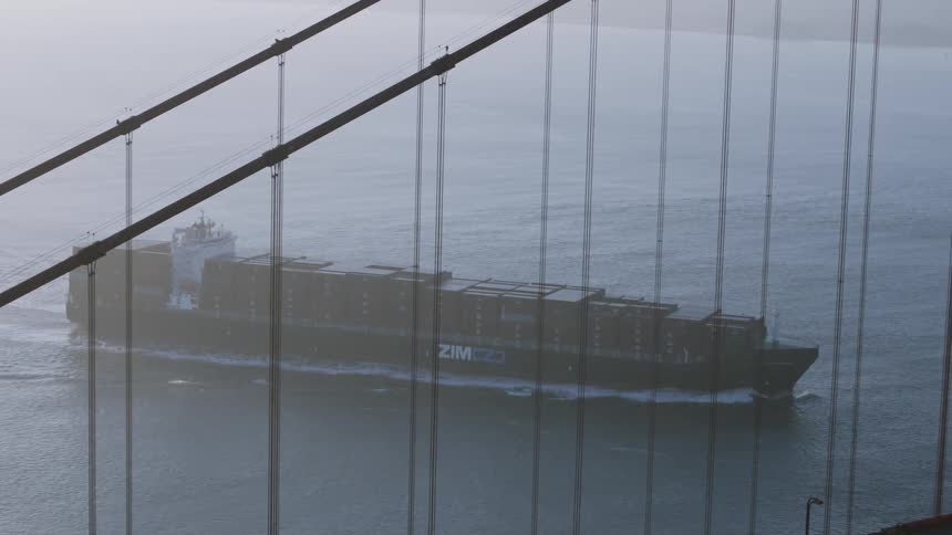 Elevated view of a barge moving along a river with a suspension bridge in the foreground