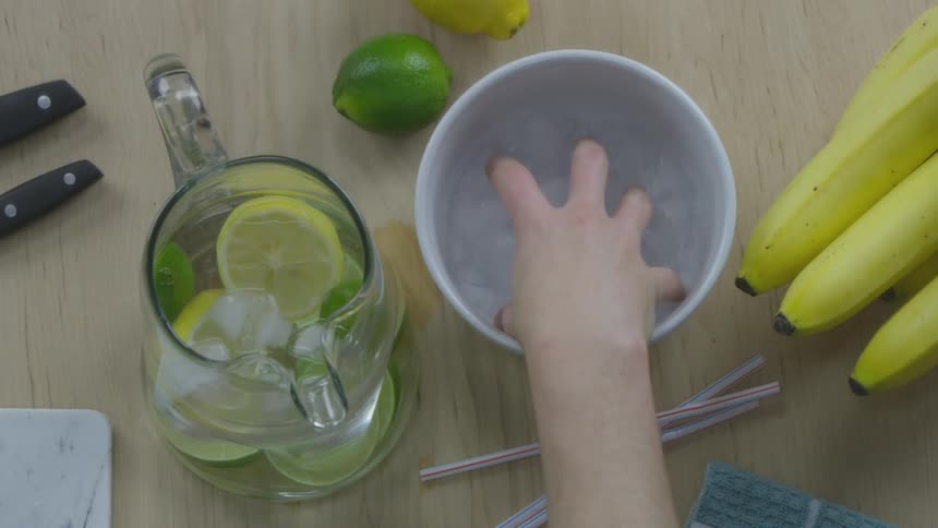 A person grabbing ice out of a bowl and putting it into a pitcher