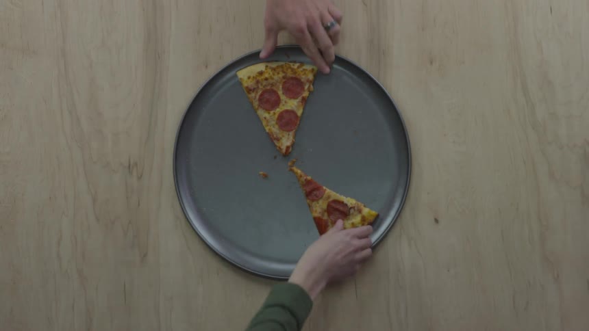 People take pizza from the plate on the wooden table