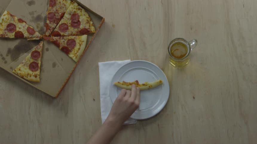 A person sets down a beverage in a glass mug and puts the crust from a slice of pizza on a white plate next to a half eaten pizza in a box